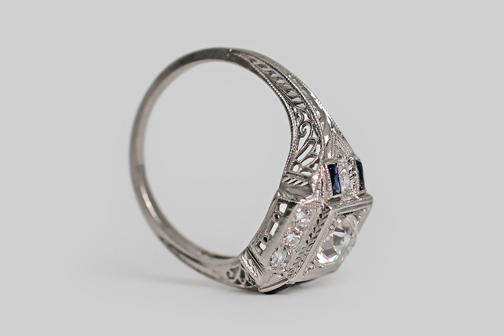 Poor Mouchette | Curated Antique Jewelry, Vintage Jewelry & Engagement Rings | Portland, Oregon | An especially fine Art Deco era engagement ring, modeled in platinum, whose primary gem is a .80 carat old European cut diamond (H/VS1). This lively, hand-cut diamond is mounted low, in a square seat, where it is held in place by trefoil beads. The primary seat is surrounded by trios of bead-set diamonds to the north and south, and pairs of diamonds to the east and west.