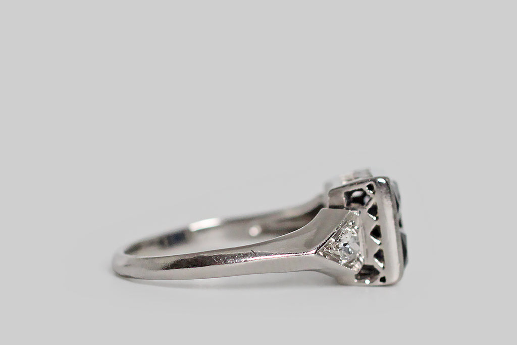 Poor Mouchette | Curated Antique Jewelry, Vintage Jewelry & Engagement Rings | Portland, Oregon | A charming Art Deco era ring, modeled in palladium, whose four, central, French cut sapphires come together to suggest an orange blossom. These deep-blue, created sapphires are set calibre-style (edge to edge) inside their large, square bezel, and a small, milgrained, palladium bead pins them, at center. The ring's square head is flanked by kite-shaped shoulders, each holding a chunky old mine cut diamond.