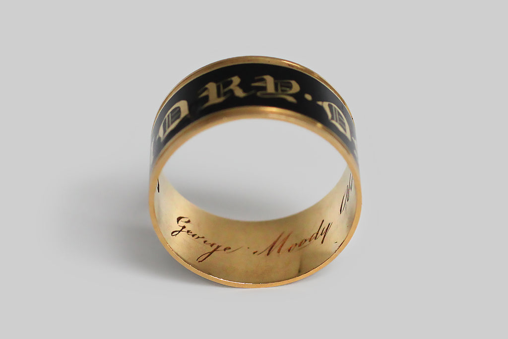 Poor Mouchette | Curated Antique Jewelry, Vintage Jewelry & Engagement Rings | Portland, Oregon | A beautiful, Georgian-era, wide band ring, modeled in 18k gold and decorated with black enamel. This broad, flat mourning band was made in memory of George Moody, and it is dated for the year 1818. This has a very subtle ribbed detail, at the lip, but its striking, clean lines are otherwise uninterrupted. The band's smooth, enameled face reads “in memory of,” in bold gothic script.