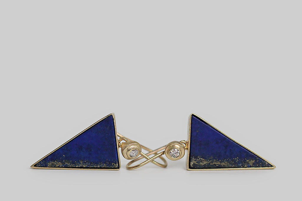 Azure-blue, triangular slabs of lapis lazuli dangle beneath a bright pair of brilliant-cut white diamonds. The diamonds are mounted in an exaggerated bezel, which is circular and subtly organic in form. The lapis triangles are matte finished, and their book-matched edges are figured with a heavy streak of golden pyrite— they're are held in full, open-back bezels, and oriented point-down so they read like arrows, darts, or bolts of lightening.