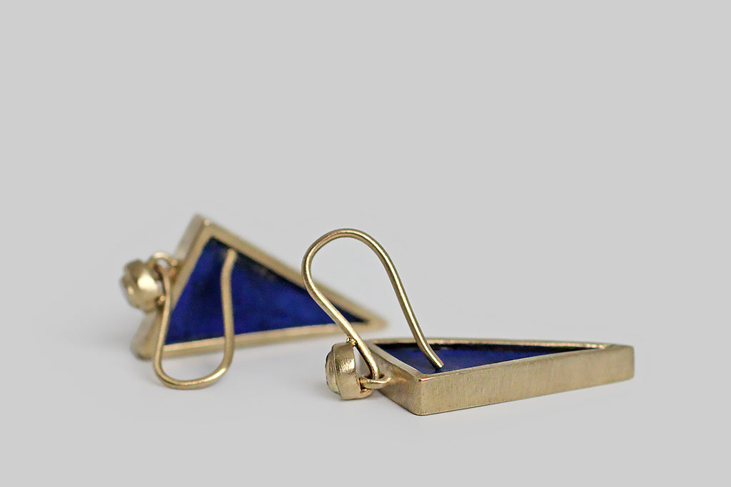 Azure-blue, triangular slabs of lapis lazuli dangle beneath a bright pair of brilliant-cut white diamonds. The diamonds are mounted in an exaggerated bezel, which is circular and subtly organic in form. The lapis triangles are matte finished, and their book-matched edges are figured with a heavy streak of golden pyrite— they're are held in full, open-back bezels, and oriented point-down so they read like arrows, darts, or bolts of lightening.