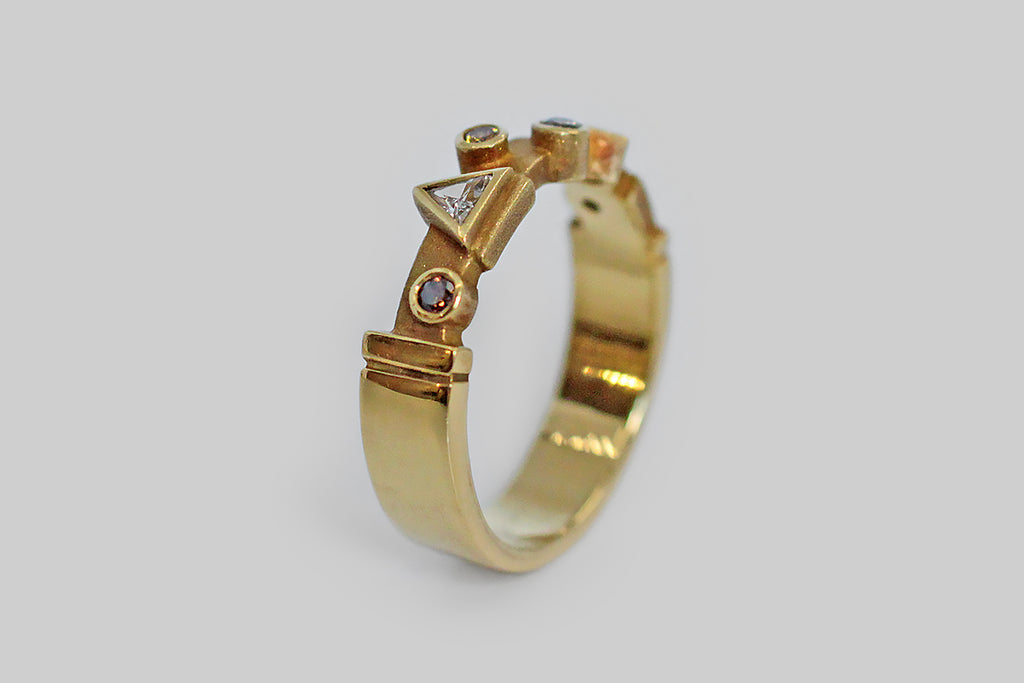 A whimsical 18k gold band, set with an array of fancy colored diamonds, in various shapes. Among these natural, bezel set stones is a cognac round brilliant diamond, two round brilliant canary diamonds, a silver colored round brilliant diamond, and two white diamonds (a triangle and a diamond shape). This playful geometric arrangement sits atop the ring's cutaway face, which has been textured for contrast and features a couple of shapely notches that I especially love. 