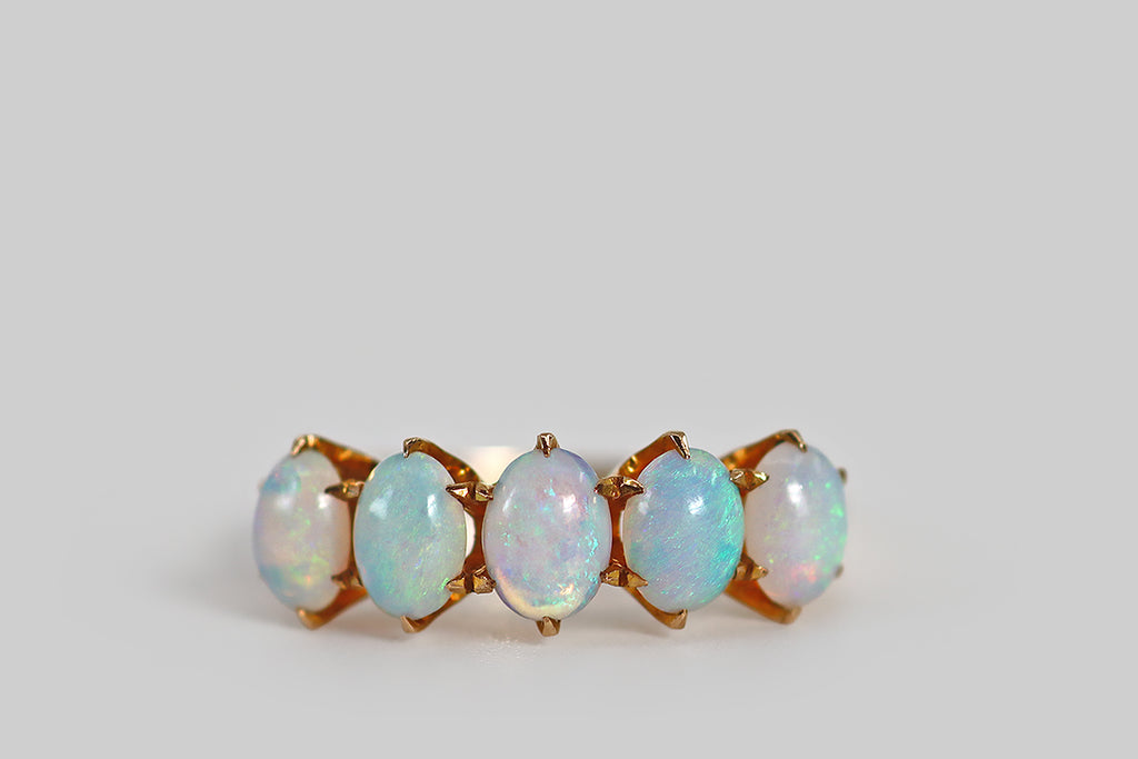 Antique Jewelry Portland, Vintage Jewelry Portland , Antique Engagement Rings | Poor Mouchette | A delicate, Victorian-era, five-stone ring, modeled in 10k rosy yellow gold, whose five natural opal cabochons are held in six-prong settings. These oval cabochons are translucent, with soft blue body tone— they display pink, blue, and green fire, in broad and ribboning patterns. The ring's slender half round shank tapers toward the base. We love the soft, ethereal aesthetic of the opals here