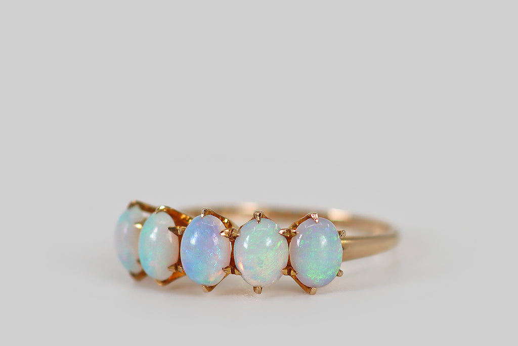Antique Jewelry Portland, Vintage Jewelry Portland , Antique Engagement Rings | Poor Mouchette | A delicate, Victorian-era, five-stone ring, modeled in 10k rosy yellow gold, whose five natural opal cabochons are held in six-prong settings. These oval cabochons are translucent, with soft blue body tone— they display pink, blue, and green fire, in broad and ribboning patterns. The ring's slender half round shank tapers toward the base. We love the soft, ethereal aesthetic of the opals here