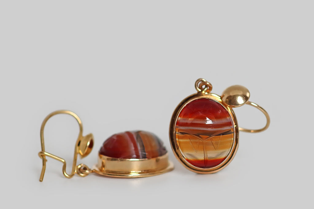 Antique Jewelry Portland, Vintage Jewelry Portland , Antique Engagement Rings | Poor Mouchette | A lovely pair of vintage dangling earrings, modeled in 14k yellow gold and set with carved banded agate cabochons. These oval cabochons have traditional carved details that transform them into scarab beetle amulets. Our agate scarabs are transparent and beautifully figured with red, orange, and black horizontal bands