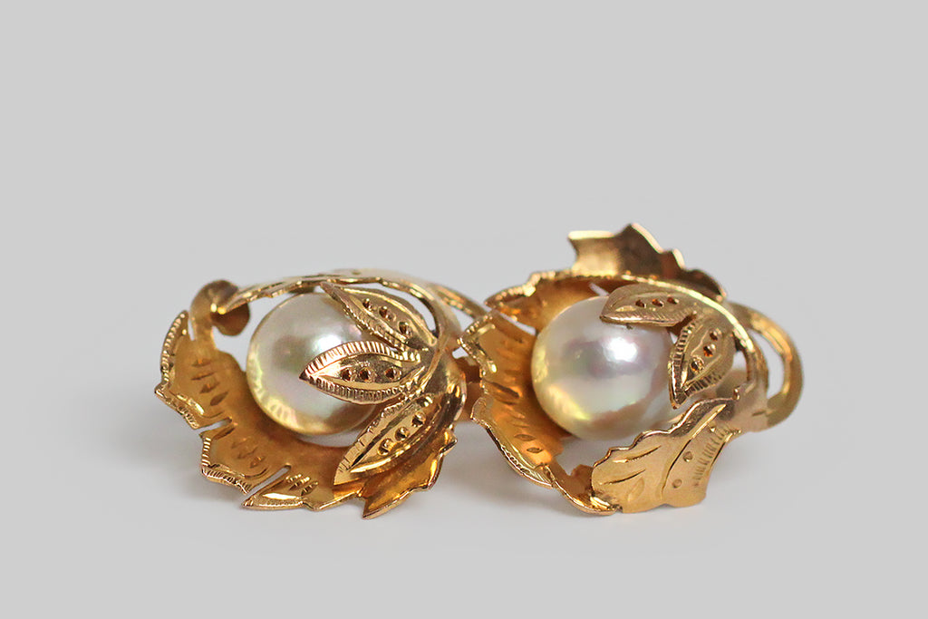 A pair of Retro era drop earrings, modeled in 18k yellow gold, whose highly-dimensional, naturalistic, folate forms were hand-pierced from gold sheet, and moulded (like a shelter) around their lustrous Akoya pearls. These leafy mounts are hand engraved and decorated with beads of granulation. The pearls they shelter read like fruit beneath the leaves