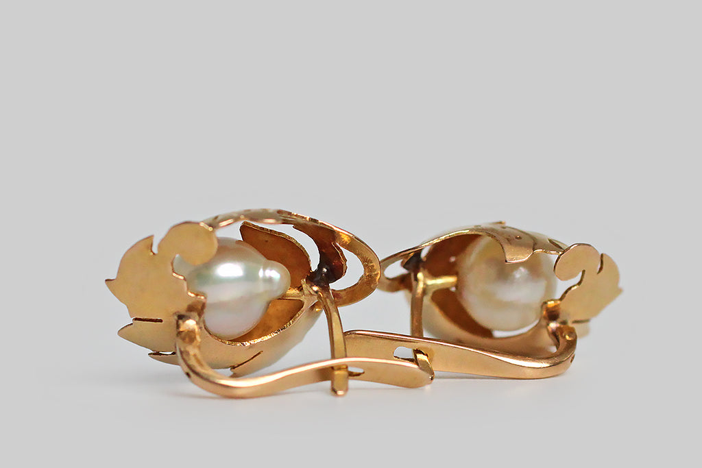 A pair of Retro era drop earrings, modeled in 18k yellow gold, whose highly-dimensional, naturalistic, folate forms were hand-pierced from gold sheet, and moulded (like a shelter) around their lustrous Akoya pearls. These leafy mounts are hand engraved and decorated with beads of granulation. The pearls they shelter read like fruit beneath the leaves