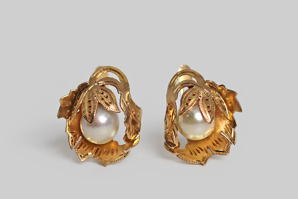 A pair of Retro era drop earrings, modeled in 18k yellow gold, whose highly-dimensional, naturalistic, folate forms were hand-pierced from gold sheet, and moulded (like a shelter) around their lustrous Akoya pearls. These leafy mounts are hand engraved and decorated with beads of granulation. The pearls they shelter read like fruit beneath the leaves