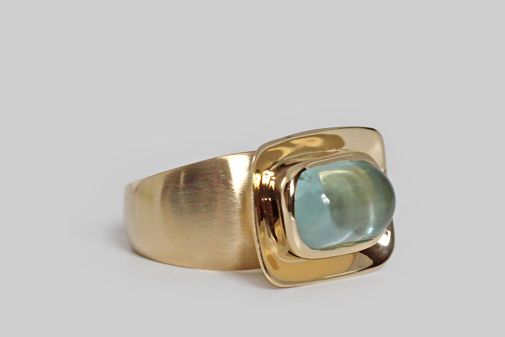 Poor Mouchette | Curated Antique Jewelry, Vintage Jewelry & Engagement Rings | Portland, Oregon | A contemporary modernist ring of our own design, featuring an anticlastic, dish-like head, and a broad, tapering, synclastic shank. A plump, lozenge-shaped, aquamarine cabochon sits at the center of the ring's softly-rectangular face, in a smooth bezel. We think this shallow platter, and it's glowing gem, give the impression of an offering (palms up)! 