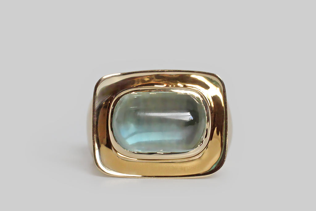Poor Mouchette | Curated Antique Jewelry, Vintage Jewelry & Engagement Rings | Portland, Oregon | A contemporary modernist ring of our own design, featuring an anticlastic, dish-like head, and a broad, tapering, synclastic shank. A plump, lozenge-shaped, aquamarine cabochon sits at the center of the ring's softly-rectangular face, in a smooth bezel. We think this shallow platter, and it's glowing gem, give the impression of an offering (palms up)!