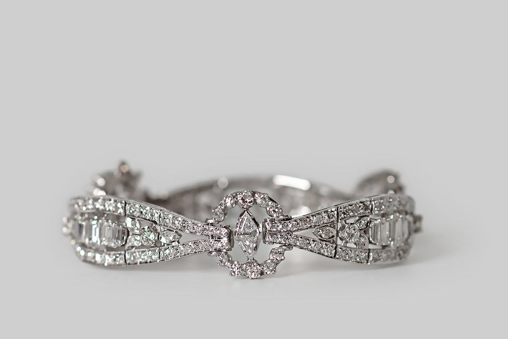 Antique Jewelry Portland, Vintage Jewelry Portland , Antique Engagement Rings | Poor Mouchette | A beautiful, Art Deco era bracelet, modeled in platinum, whose three diamond-set rosettes are joined by the long, tapering, diamond-set bands that stretch between them. These jointed, sash-like bands each feature five, emerald cut diamonds, that graduate in size. Round and marquise shaped seats create the impression of diamond leaves and berries, flanking these step cuts