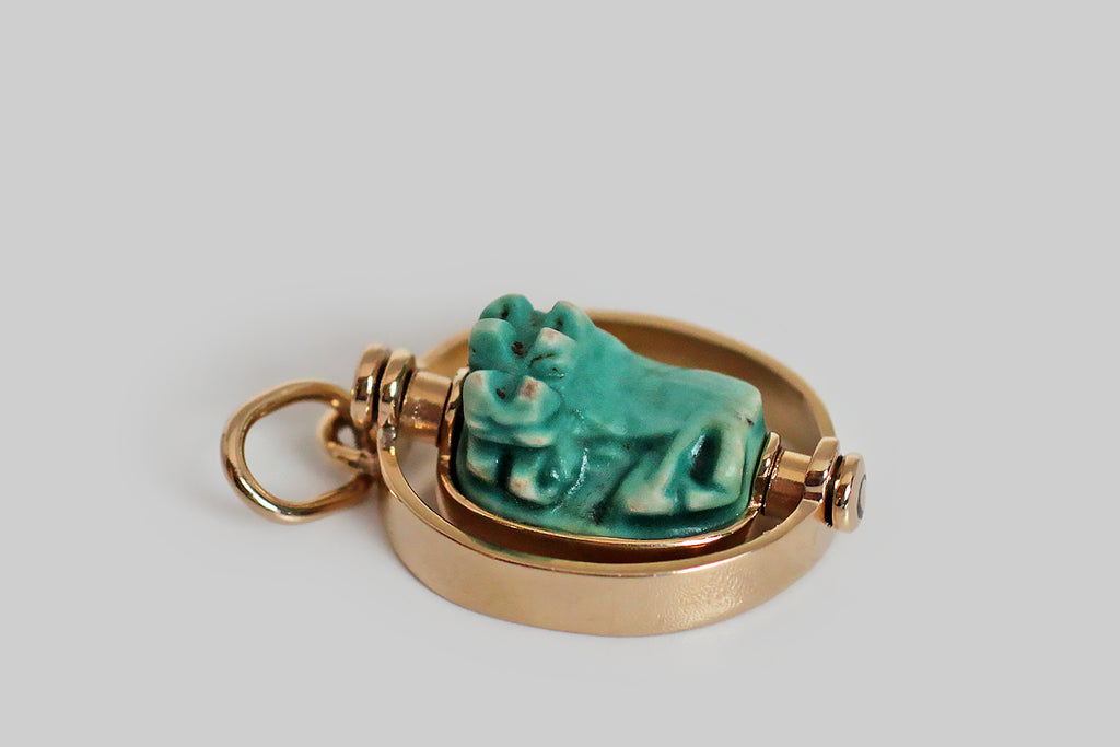 Poor Mouchette | Curated Antique Jewelry, Vintage Jewelry & Engagement Rings | Portland, Oregon | A charming Art Deco era pendant, modeled in 14k yellow gold, whose centerpiece is an Egyptian faience bead that rotates inside the pendant's oval, flat-wire frame. The glazed, blue-green, faience bead is crowned with a three-dimensional likeness of a hippopotamus— the little beast lounges on a pedestal, with her legs outstretched, and she seems to be smiling. The goddess Taweret