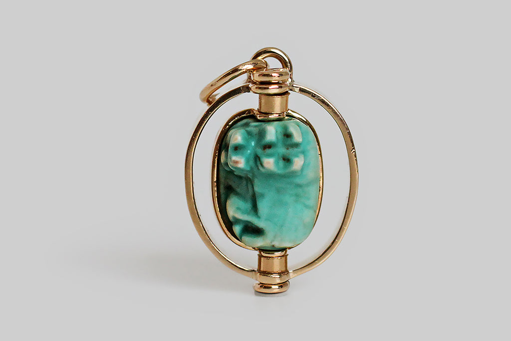 Poor Mouchette | Curated Antique Jewelry, Vintage Jewelry & Engagement Rings | Portland, Oregon | A charming Art Deco era pendant, modeled in 14k yellow gold, whose centerpiece is an Egyptian faience bead that rotates inside the pendant's oval, flat-wire frame. The glazed, blue-green, faience bead is crowned with a three-dimensional likeness of a hippopotamus— the little beast lounges on a pedestal, with her legs outstretched, and she seems to be smiling. The goddess Taweret
