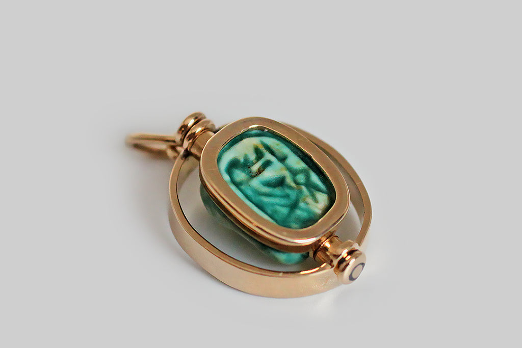 Poor Mouchette | Curated Antique Jewelry, Vintage Jewelry & Engagement Rings | Portland, Oregon | A charming Art Deco era pendant, modeled in 14k yellow gold, whose centerpiece is an Egyptian faience bead that rotates inside the pendant's oval, flat-wire frame. The glazed, blue-green, faience bead is crowned with a three-dimensional likeness of a hippopotamus— the little beast lounges on a pedestal, with her legs outstretched, and she seems to be smiling. The goddess Taweret