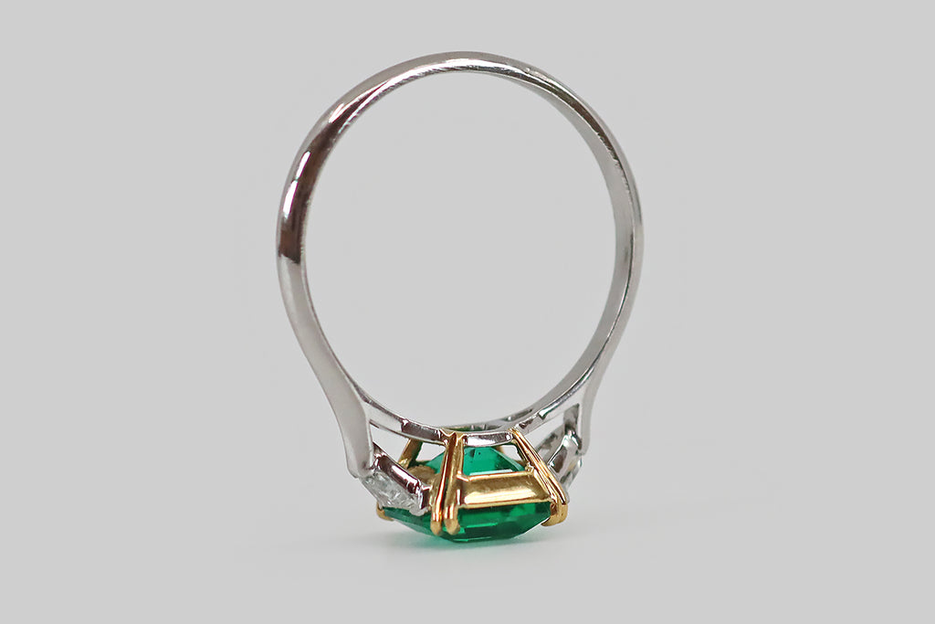 Antique Jewelry Portland, Vintage Jewelry Portland , Antique Engagement Rings | Poor Mouchette | An elegant Art Deco era engagement ring, modeled in platinum and 18k yellow gold, whose primary gem is an especially fine Colombian emerald (approx 1.9 carats). This square, step cut emerald has that most covetable, vivid, deep-bluish-green hue and remarkable transparency— it glows atop the ring's face, where it rests in a yellow gold basket.