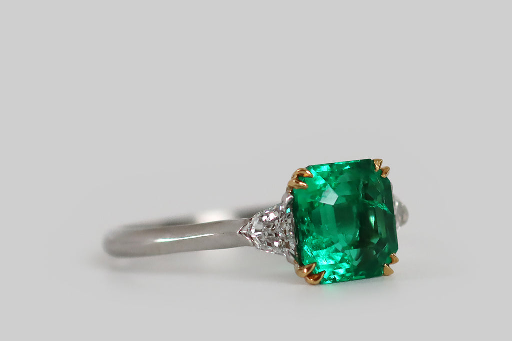 Antique Jewelry Portland, Vintage Jewelry Portland , Antique Engagement Rings | Poor Mouchette | An elegant Art Deco era engagement ring, modeled in platinum and 18k yellow gold, whose primary gem is an especially fine Colombian emerald (approx 1.9 carats). This square, step cut emerald has that most covetable, vivid, deep-bluish-green hue and remarkable transparency— it glows atop the ring's face, where it rests in a yellow gold basket.