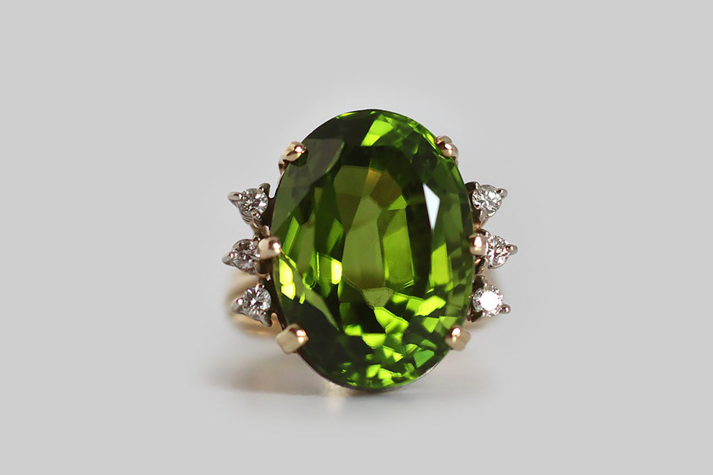 A glamourous, vintage, 1960s cocktail ring, featuring a big, exceptional, once in a lifetime, Burmese peridot. This gem is highly-saturated, grass green, and crystal clear— its weight is approximately 19 carats. The peridot is held aloft in an 18k yellow gold setting, whose open, cage-like shape is iconic of the period. Three, round, brilliant-cut, white diamonds adorn either side of the rare central gemstone. The GIA refers to peridot as "the extreme gem," because it is one of only two gemstones (diamond