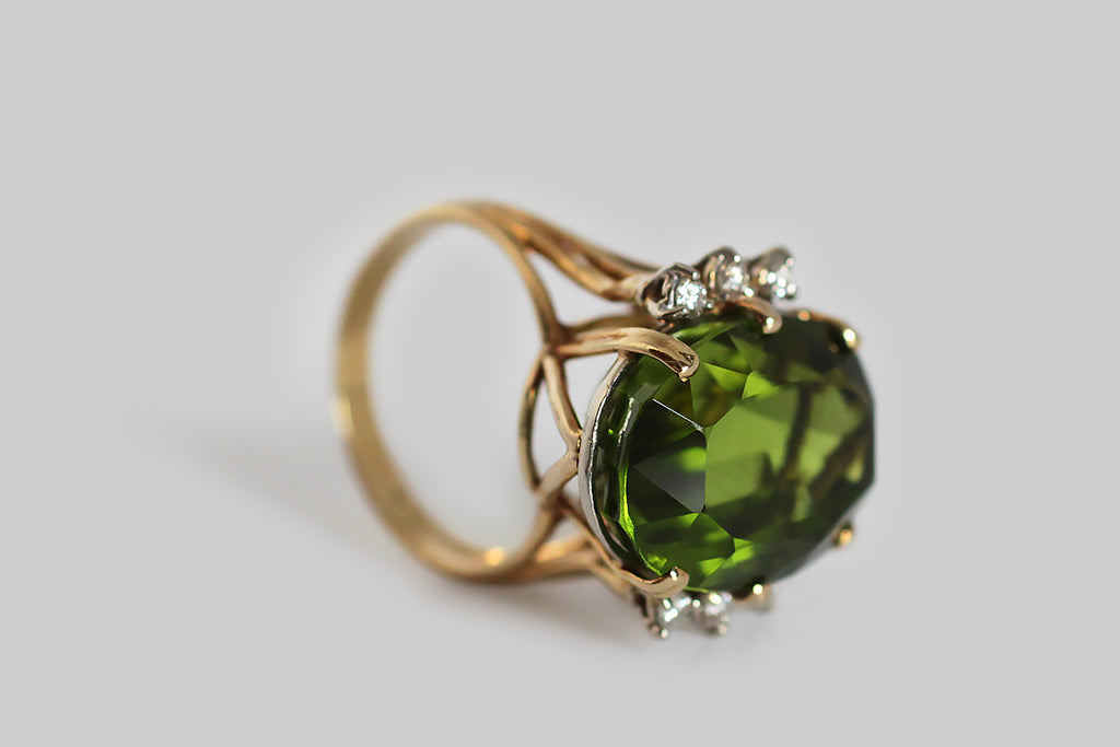 A glamourous, vintage, 1960s cocktail ring, featuring a big, exceptional, once in a lifetime, Burmese peridot. This gem is highly-saturated, grass green, and crystal clear— its weight is approximately 19 carats. The peridot is held aloft in an 18k yellow gold setting, whose open, cage-like shape is iconic of the period. Three, round, brilliant-cut, white diamonds adorn either side of the rare central gemstone. The GIA refers to peridot as "the extreme gem," because it is one of only two gemstones (diamond i