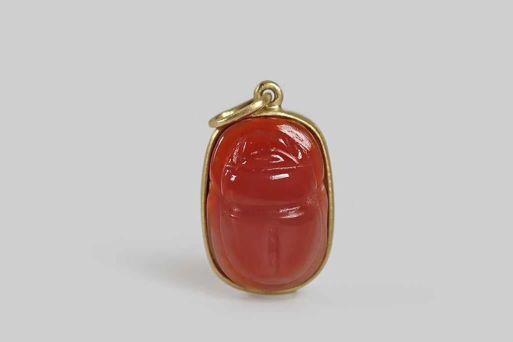 Antique Jewelry Portland, Vintage Jewelry Portland , Antique Engagement Rings | Poor Mouchette | A charming pendant, modeled in 18k yellow, that features a vintage carnelian cabochon, carved to represent a scarab beetle. This carnelian is softer and a bit rosier than usual, and the scarab carving is especially well-executed, with attractive proportions and polished edges— it is smooth, semi-translucent, and glowy!