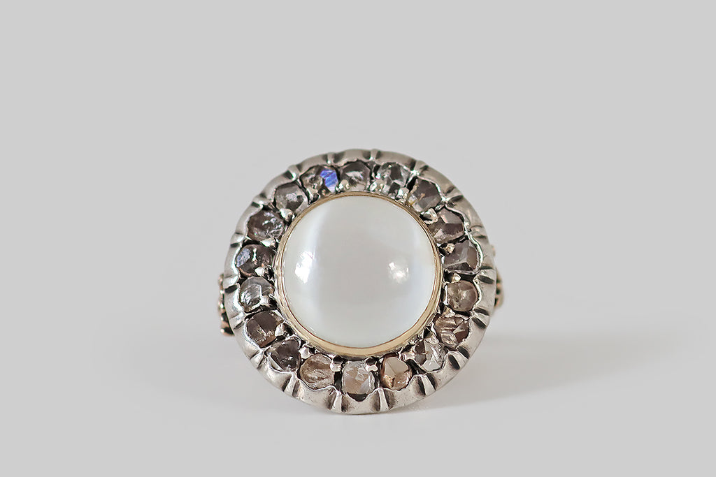 Antique Jewelry Portland, Vintage Jewelry Portland , Antique Engagement Rings | Poor Mouchette | A wonderful, unusual, Edwardian era ring, modeled in rose gold and silver, whose primary gem is a large, round, cat's eye moonstone cabochon. This white moonstone is set in a low-profile, rose gold bezel, where it is surrounded by a halo of eighteen, natural, rose cut diamonds— it has a prominent, glowing, vertical eye that shifts with movement! The old rose cut diamonds