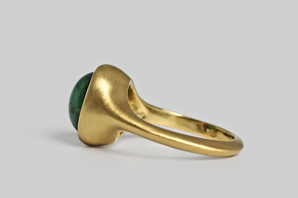Glowing and vibrant, a highly-saturated, a teal-green tourmaline cabochon sits, nested, inside a thick-walled, organic bezel, which tapers seamlessly into the ring's integral shank. This elegant, oval, tourmaline gem exhibits the rare and beautiful cats eye phenomenon, known as chatoyancy, which gives the stone a two color 