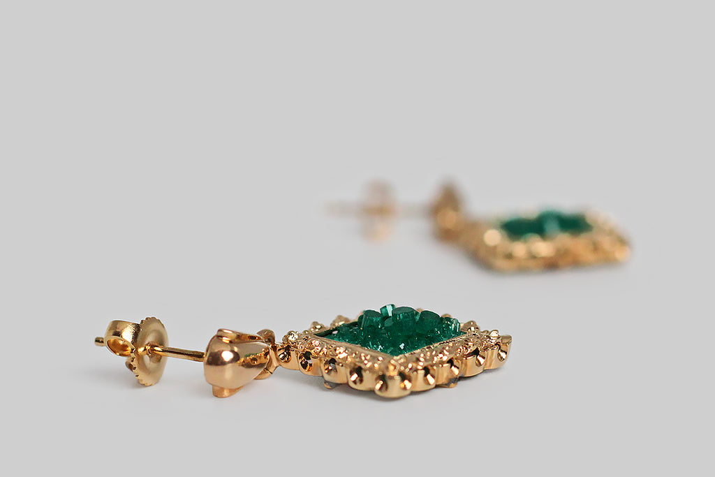 A wonderful, unusual pair of vintage earrings, modeled in 14k yellow gold, featuring square slabs of vibrant, uncut, bedding, Chatham emerald crystals. Because these created emeralds are still in their raw form, the vibrant green beds are populated by small, sparkling crystals of various heights! These beautiful Chatham specimens are set in “picture frame” mounts, which are oriented in a diamond shape. 