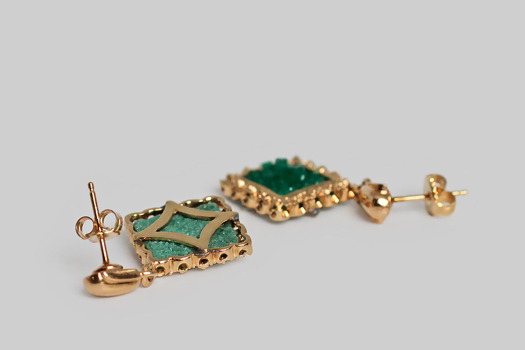 A wonderful, unusual pair of vintage earrings, modeled in 14k yellow gold, featuring square slabs of vibrant, uncut, bedding, Chatham emerald crystals. Because these created emeralds are still in their raw form, the vibrant green beds are populated by small, sparkling crystals of various heights! These beautiful Chatham specimens are set in “picture frame” mounts, which are oriented in a diamond shape. 