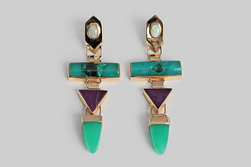 A pair of long, late-vintage drop earrings, modeled in 14k yellow gold, whose playful form concerns itself with shape and color. These earrings feature four types of colorful, bezel-set, cabochon gemstones — white opal, chrysocolla, sugilite, and chrysoprase — these vibrant stones are arranged in a vertical row of chunky geometric shapes. The 14k bezels are beautifully made, and hinged together, so that they swing back and forth with movement. These earrings are entirely hand fabricated. 