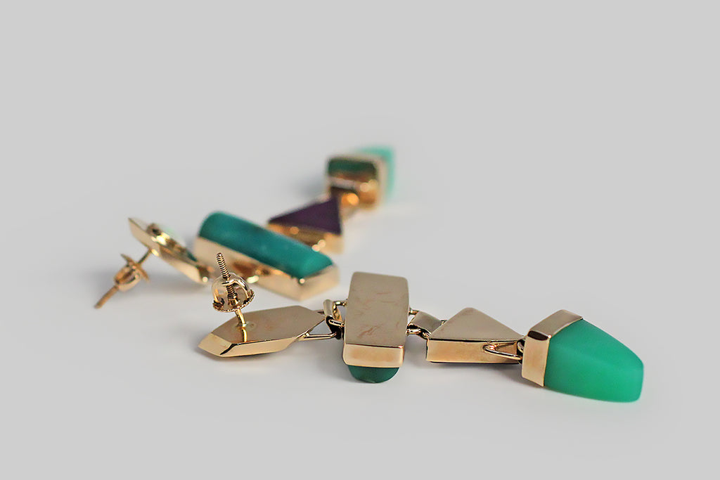 A pair of long, late-vintage drop earrings, modeled in 14k yellow gold, whose playful form concerns itself with shape and color. These earrings feature four types of colorful, bezel-set, cabochon gemstones — white opal, chrysocolla, sugilite, and chrysoprase — these vibrant stones are arranged in a vertical row of chunky geometric shapes. The 14k bezels are beautifully made, and hinged together, so that they swing back and forth with movement. These earrings are entirely hand fabricated. 