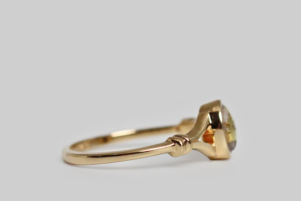 A dainty vintage ring, modeled in 14k yellow gold, featuring a small, oval, gold-in-quartz cabochon. This bezel-set, gold-bearing quartz gem is heavily figured with natural gold, presenting as swaths of vibrant yellow that seem to paint its surface. The ring’s thick-walled bezel floats inside its split shoulders. The shoulders are decorated with a simple banded detail, that makes them appear bound together. The ring's shank is substantial and softly square. 
