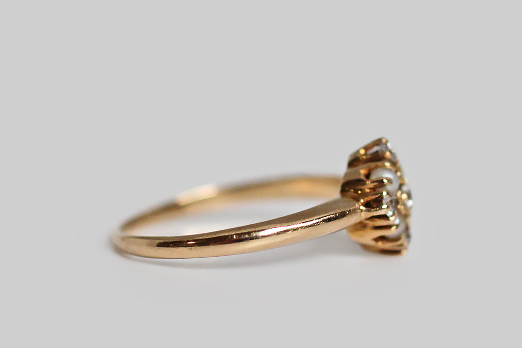A late Victorian diamond and seed pearl cluster ring, with outstanding proportion and balance. This dainty love is modeled in 14k yellow gold. Its head is a thoughtfully-made, equilateral diamond, that holds within it the ring's five white diamonds and four natural seed pearls. There is a subtle cruciform shape implied by the diamond layout, and the ring's centermost prongs come together to give the impression of small flowers. The ring's  integral, half-round shank tapers toward the base. 