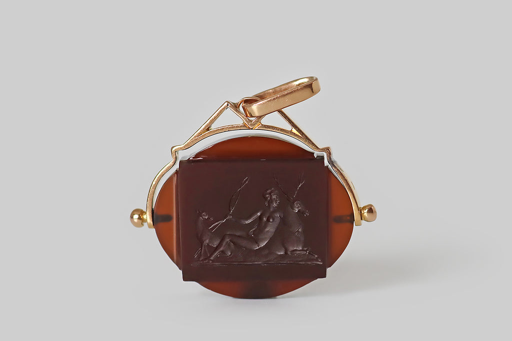 Antique Jewelry Portland, Vintage Jewelry Portland , Antique Engagement Rings | Poor Mouchette | A wonderful Victorian-era pendant, modeled in 14k rosy yellow gold, whose oval slab of red-brown sard features an intaglio carving of Diana the huntress, lounging with her stag and hound! This beautiful scene is carved onto the gem's rectangular “table," which stands slightly proud of the larger oval shape, overlapping it slightly at the corners. The image closely approximates the Diana of Anet