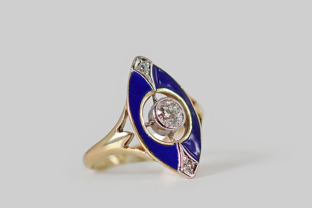 Poor Mouchette | Curated Antique Jewelry, Vintage Jewelry & Engagement Rings | Portland, Oregon | A charming Edwardian era ring, modeled in 14k gold, whose navette-shaped face is decorated with glassy, cobalt-blue enamel. This petite navette has a circular opening at its center, where a sparkling, 1/3 carat, old mine cut diamond rests in a "floating" platinum bezel. A pair of shapely, diamond-set, platinum forms accent the north and south points of the ring face, reading like plumes extending