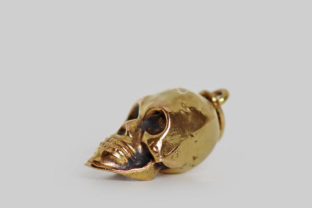 Poor Mouchette | Curated Antique Jewelry, Vintage Jewelry & Engagement Rings | Portland, Oregon | A rare and wonderful, miniature, early-20th-century charm, modeled in 14k gold, that takes the form of an especially handsome human skull! This antique skull charm is a partly hollow cast, with deep eye cavities, prominent cheek bones, a sharp jawbone, and two full rows of teeth. Patches of black patina give this gruesome old gent extra dimensionality and authenticity. He is a beautiful, weathered specimen!