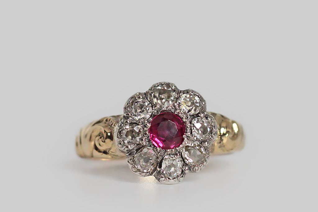 A soulful, Georgian-era, flower-form ring, modeled in 18k yellow gold with a silver top. This ring’s eight, oval, collet-set, old mine cut diamonds are arranged around its vibrant, untreated, central ruby. The shoulders of the ring are decorated with voluptuous, swirling repoussé work, that is typical of the period. This ring has a closed back, and its weighty, half-round shank tapers toward the base. 