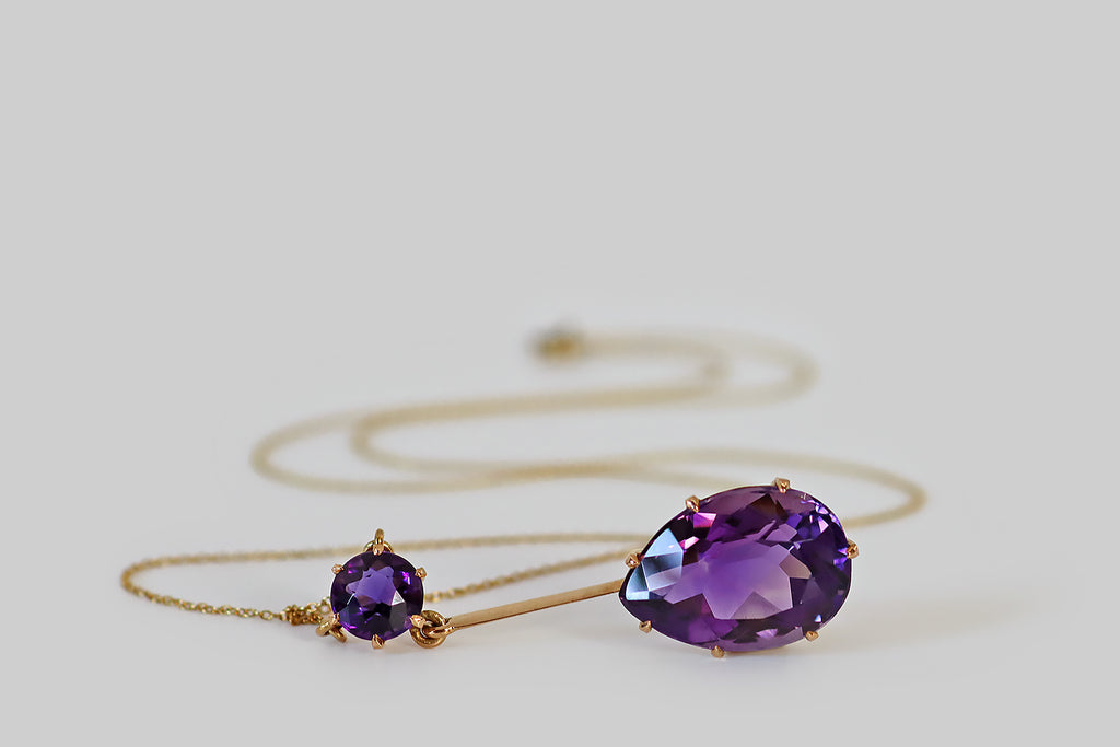 Antique Jewelry Portland, Vintage Jewelry Portland , Antique Engagement Rings | Poor Mouchette | An elegant, Edwardian-era lavalier necklace, modeled in 14k gold, whose focal element is a large, faceted pear shaped amethyst. This lovely faceted pear drops from a single, smaller, amethyst round— a long, slender, knife-edge bar connects the two gems. These old amethysts are a highly-saturated, deep, cool-tone purple.