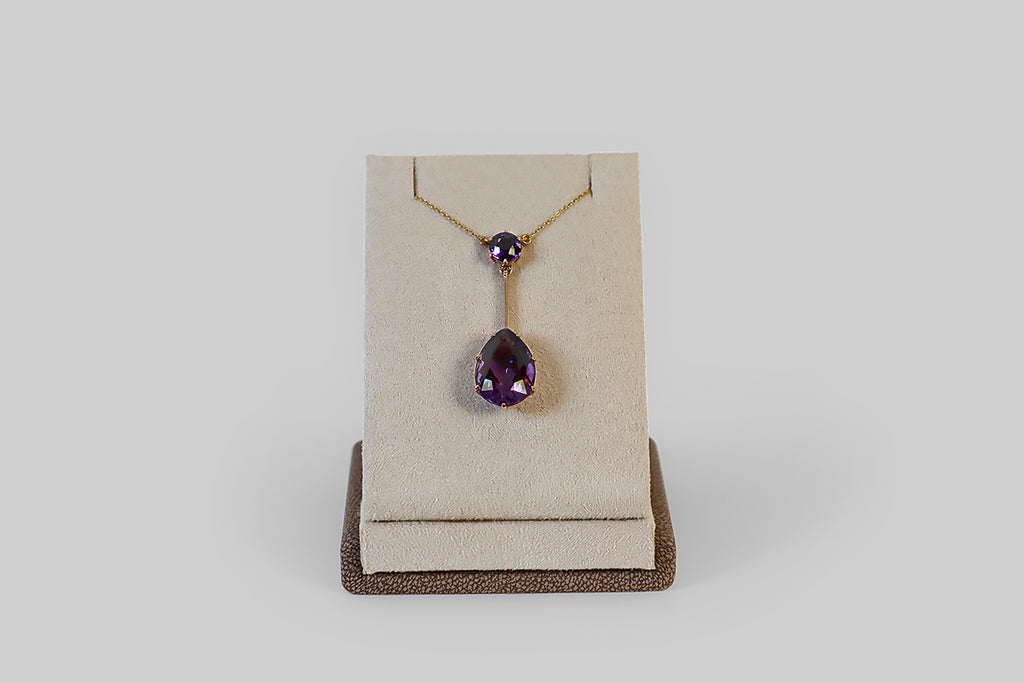 Antique Jewelry Portland, Vintage Jewelry Portland , Antique Engagement Rings | Poor Mouchette | An elegant, Edwardian-era lavalier necklace, modeled in 14k gold, whose focal element is a large, faceted pear shaped amethyst. This lovely faceted pear drops from a single, smaller, amethyst round— a long, slender, knife-edge bar connects the two gems. These old amethysts are a highly-saturated, deep, cool-tone purple.