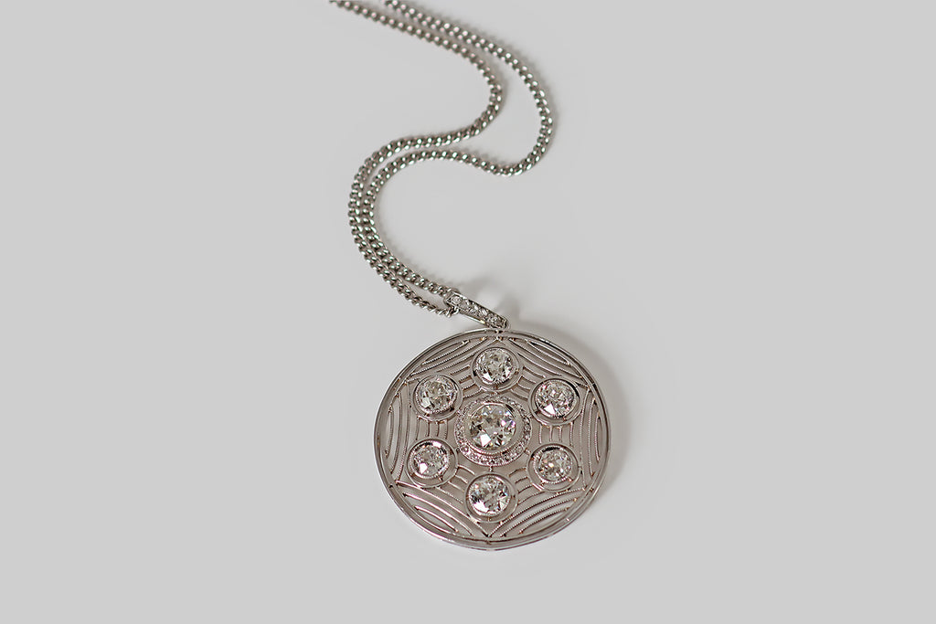 Antique Jewelry Portland, Vintage Jewelry Portland , Antique Engagement Rings | Poor Mouchette | A striking Art Deco era pendant, modeled in platinum, whose fine, hand-fabricated filigree forms a spider's web inside of the pendant's circular frame. Seven, sparkling old mine cut diamonds are "caught" in this web. The primary diamond is approx .93 carats— it rests in a mirror edge bezel, surrounded a halo of small rose cut diamonds.