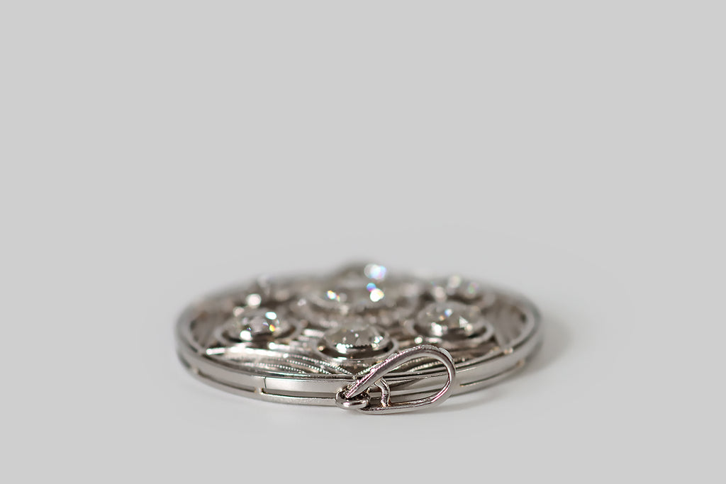 Antique Jewelry Portland, Vintage Jewelry Portland , Antique Engagement Rings | Poor Mouchette | A striking Art Deco era pendant, modeled in platinum, whose fine, hand-fabricated filigree forms a spider's web inside of the pendant's circular frame. Seven, sparkling old mine cut diamonds are "caught" in this web. The primary diamond is approx .93 carats— it rests in a mirror edge bezel, surrounded a halo of small rose cut diamonds.