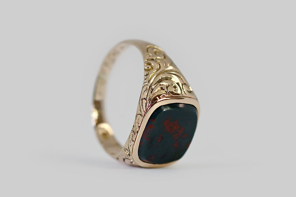 Antique Jewelry Portland, Vintage Jewelry Portland , Antique Engagement Rings | Poor Mouchette | An Edwardian era signet ring, modeled in 10k rosy yellow gold, whose gem is a striking bloodstone slab. This beautifully figured bloodstone specimen has a beveled edge. It is set in a smooth, low-profile bezel. Its dark green (almost black) field is marked with a spattering of well-defined, vibrant red flecks that read like blood splattered across the surface of a rock.