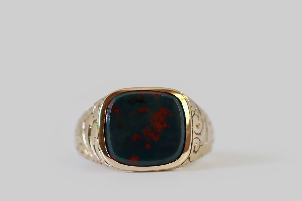 Antique Jewelry Portland, Vintage Jewelry Portland , Antique Engagement Rings | Poor Mouchette | An Edwardian era signet ring, modeled in 10k rosy yellow gold, whose gem is a striking bloodstone slab. This beautifully figured bloodstone specimen has a beveled edge. It is set in a smooth, low-profile bezel. Its dark green (almost black) field is marked with a spattering of well-defined, vibrant red flecks that read like blood splattered across the surface of a rock. 