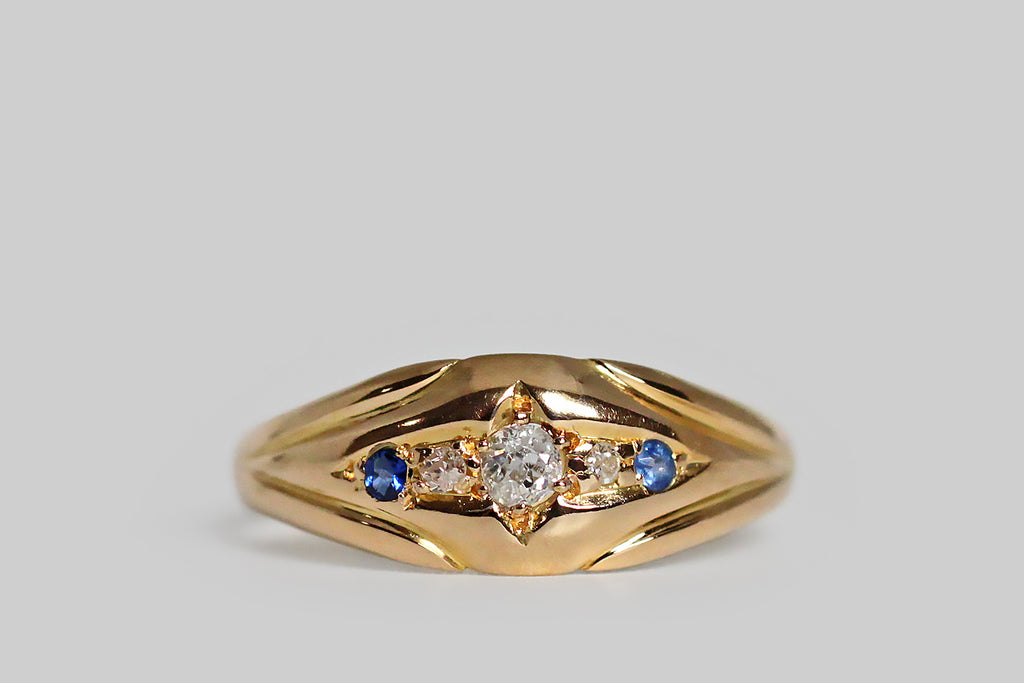Poor Mouchette | Curated Antique Jewelry, Vintage Jewelry & Engagement Rings | Portland, Oregon | A charming, Edwardian-era, five stone ring, modeled in 18k yellow gold, with an elegant, tapering profile. This antique band is carved so that its face appears slightly recessed and nested inside the split, palm-like decor of its shoulders. At center, a shapely, four-pointed, lanceolate channel holds the ring’s five gemstones— three chunky old mine cut diamonds and a petite pair of natural blue sapphires.