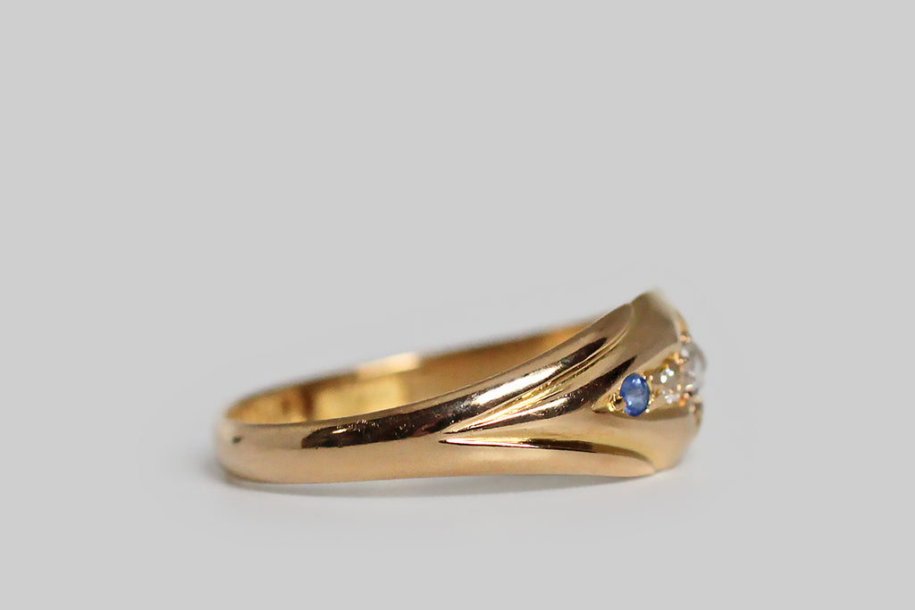Poor Mouchette | Curated Antique Jewelry, Vintage Jewelry & Engagement Rings | Portland, Oregon | A charming, Edwardian-era, five stone ring, modeled in 18k yellow gold, with an elegant, tapering profile. This antique band is carved so that its face appears slightly recessed and nested inside the split, palm-like decor of its shoulders. At center, a shapely, four-pointed, lanceolate channel holds the ring’s five gemstones— three chunky old mine cut diamonds and a petite pair of natural blue sapphires.