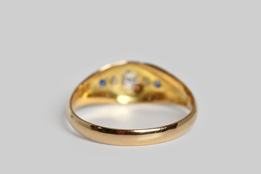 Poor Mouchette | Curated Antique Jewelry, Vintage Jewelry & Engagement Rings | Portland, Oregon | A charming, Edwardian-era, five stone ring, modeled in 18k yellow gold, with an elegant, tapering profile. This antique band is carved so that its face appears slightly recessed and nested inside the split, palm-like decor of its shoulders. At center, a shapely, four-pointed, lanceolate channel holds the ring’s five gemstones— three chunky old mine cut diamonds and a petite pair of natural blue sapphires.