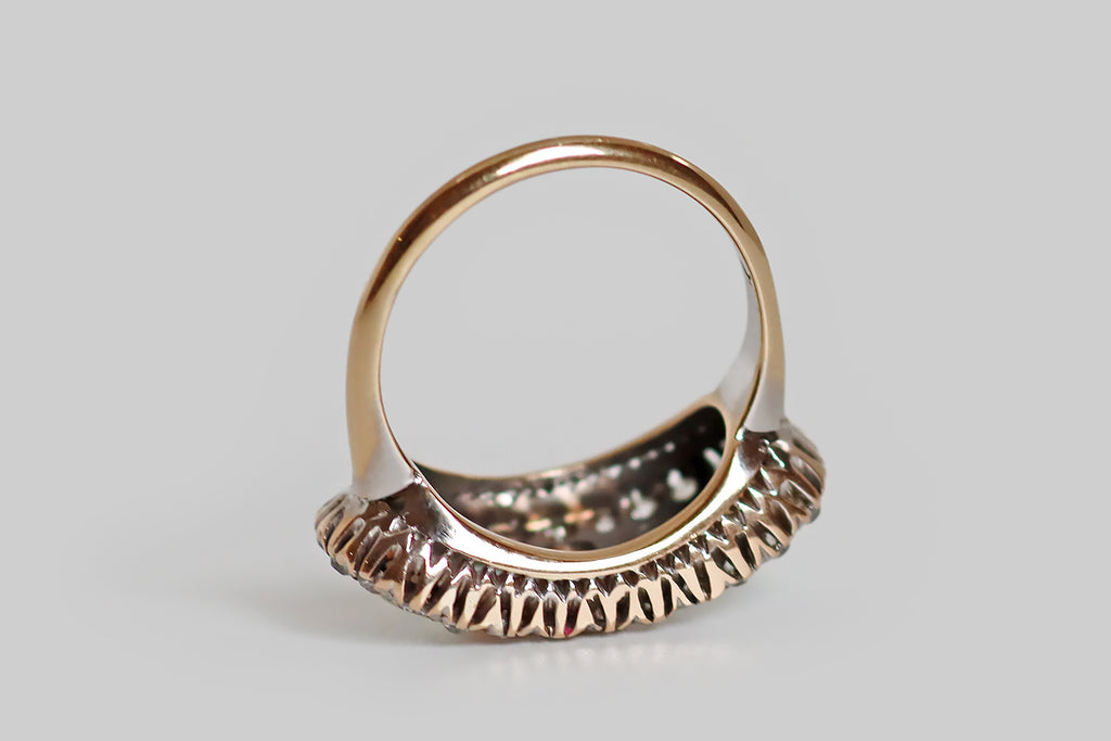 An elegant antique five stone ring, modeled in 14k rose gold, whose primary gems are a series of fiery white opals. These opal cabochons graduate in size across the ring's long, east/west oriented face, which is gently bowed. A border of glittering old cut diamonds, mounted in notched, fishtail settings, surrounds the five opals— the ring's gallery is a decoratively pierced extension of this diamond surround.