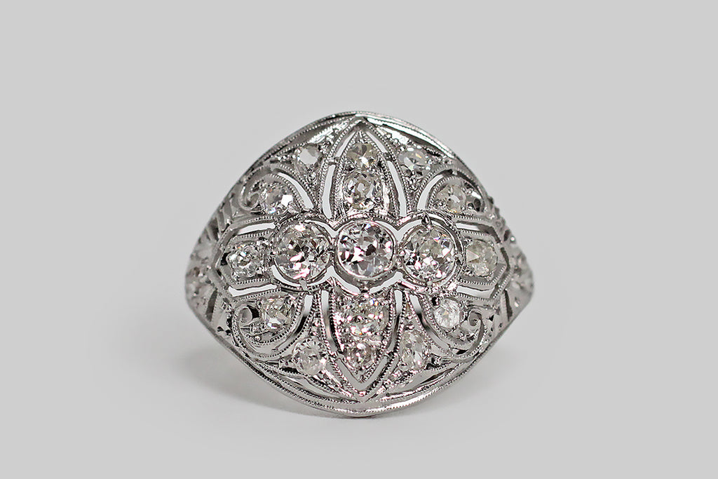 Poor Mouchette | Curated Antique Jewelry, Vintage Jewelry & Engagement Rings | Portland, Oregon | An elegant, early Art Deco diamond cluster ring with Edwardian sensibilities, modeled in 18k white gold with a platinum top. This glamorous, low-profile ring covers the finger like a rounded, tapering shield. It features lovely, hand-pierced decor, that covers the shield-like ring face from edge to edge— the central decor element, here, is a shapely fleur de lis.