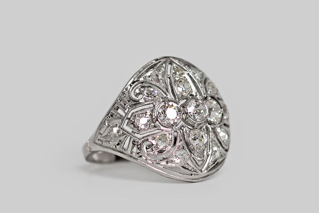 Poor Mouchette | Curated Antique Jewelry, Vintage Jewelry & Engagement Rings | Portland, Oregon | An elegant, early Art Deco diamond cluster ring with Edwardian sensibilities, modeled in 18k white gold with a platinum top. This glamorous, low-profile ring covers the finger like a rounded, tapering shield. It features lovely, hand-pierced decor, that covers the shield-like ring face from edge to edge— the central decor element, here, is a shapely fleur de lis.