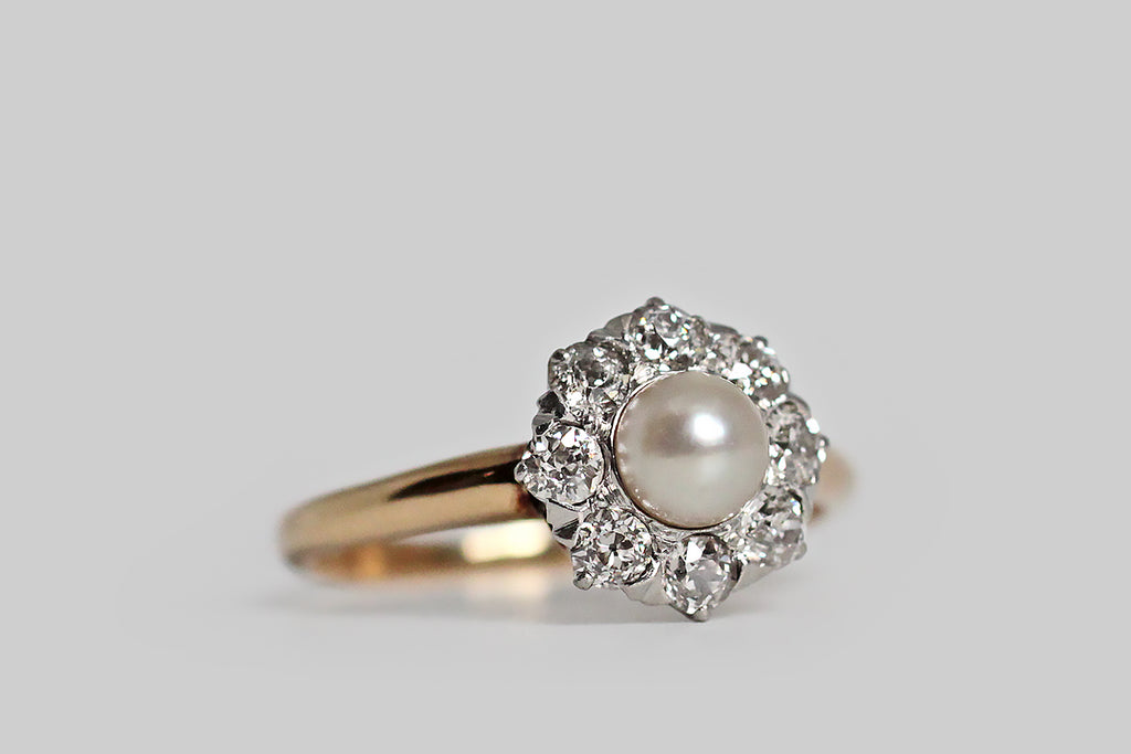 Poor Mouchette | Curated Antique Jewelry, Vintage Jewelry & Engagement Rings | Portland, Oregon | An especially winning example of a classic style, this Edwardian-era pearl and diamond halo ring, modeled in rosy 14k and platinum, has beautiful proportions! The ring’s central, luminous, champagne-white pearl is set in a fitted cup— it surrounded by a halo of eight, chunky, old European cut diamonds. These soulful, hand-cut diamonds are set into the ring's crownlike head
