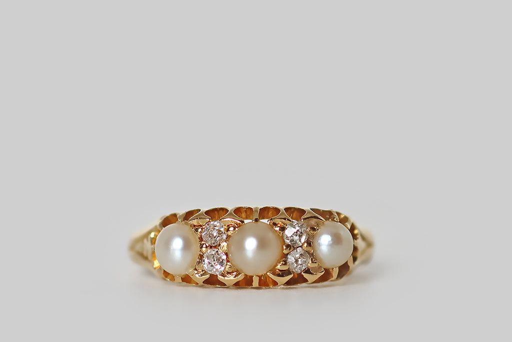 Poor Mouchette | Curated Antique Jewelry, Vintage Jewelry & Engagement Rings | Portland, Oregon | A dainty, Edwardian-era three stone ring, modeled in 18k yellow gold, and set with a trio of luminous, natural pearls. These three half-pearls are held in a series of modified, claw-like prongs that are integral to the ring's classic, scalloped, belcher-style gallery. Pairs of little old mine cut diamonds lay between our creamy pearls, and a single engraved leaf graces each of the ring's shoulders.
