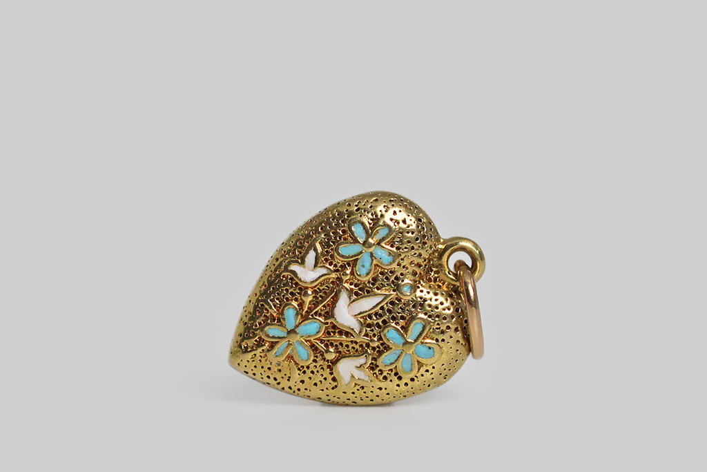 A darling, Art Deco era, heart-shaped harm, modeled in 14k yellow gold, and decorated with flowers in blue and white enamel. These little blossoms (lilies of the valley and forget me nots) sit atop the charm's finely-speckled, hand-textured surface. 